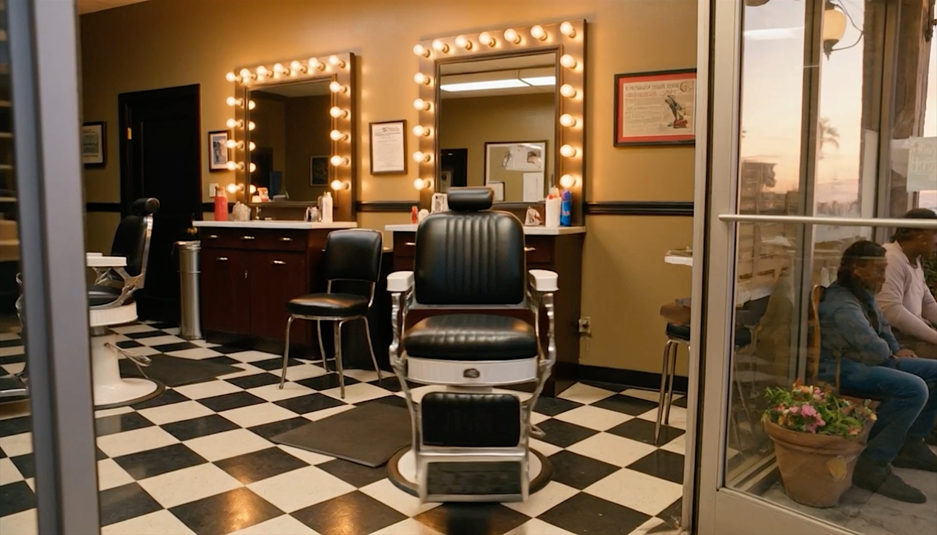 Inside the shop: a vintage black-and-chrome barber chair on a checkerboard floor, mirrors ringed with warm bulbs.